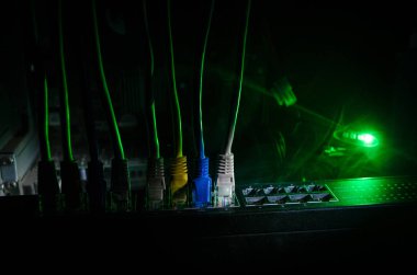 Ağ anahtarı ve ethernet kabloları, global iletişim sembolüdür. Işıklar ve duman ile koyu arka plan üzerinde renkli ağ kabloları. Seçici odak
