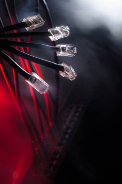 Ağ anahtarı ve ethernet kabloları, global iletişim sembolüdür. Işıklar ve duman ile koyu arka plan üzerinde renkli ağ kabloları. Seçici odak