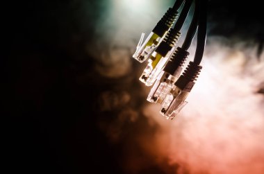 Ağ anahtarı ve ethernet kabloları, global iletişim sembolüdür. Işıklar ve duman ile koyu arka plan üzerinde renkli ağ kabloları. Seçici odak