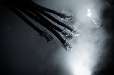 Ağ anahtarı ve ethernet kabloları, global iletişim sembolüdür. Işıklar ve duman ile koyu arka plan üzerinde renkli ağ kabloları. Seçici odak
