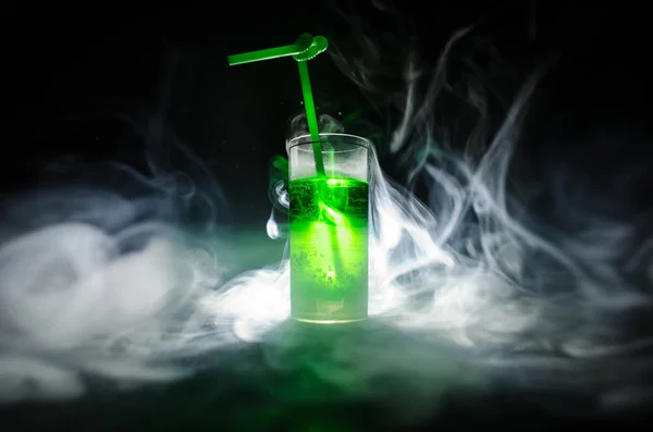 Vaso de cóctel verde con paja sobre fondo oscuro con humo y contraluz . — Foto de Stock