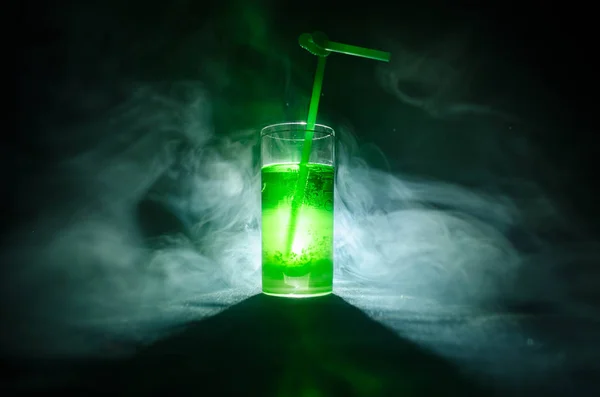 Vaso de cóctel verde con paja sobre fondo oscuro con humo y contraluz . — Foto de Stock