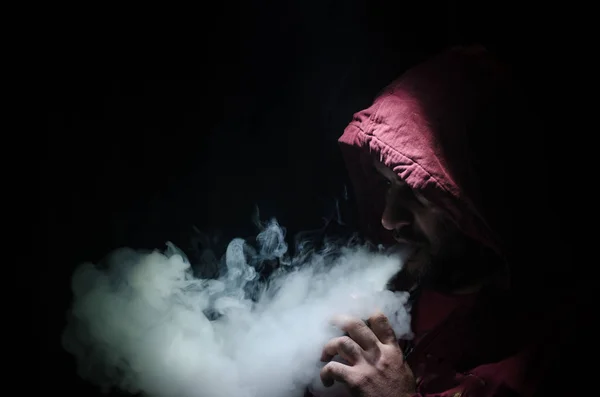 Vaping άνθρωπος που κρατά ένα mod. Ένα σύννεφο των ατμού. Μαύρο φόντο. Ηλεκτρονικό τσιγάρο με πολύ καπνό καπνίσματος — Φωτογραφία Αρχείου