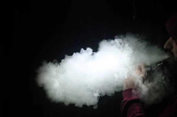 Vaping man met een mod. Een wolk van damp. Zwarte achtergrond. Vaping een elektronische sigaret met veel rook — Stockfoto