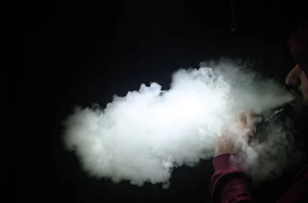 Vaping man holding a mod. A cloud of vapor. Black background. Vaping an electronic cigarette with a lot of smoke — Stock Photo, Image