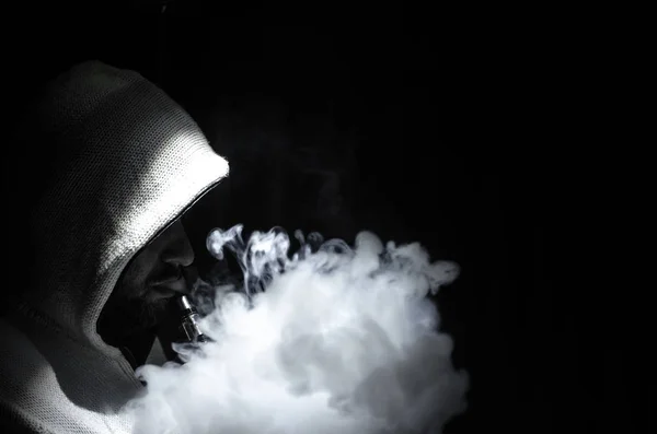 Hombre aspirante sosteniendo un mod. Una nube de vapor. Fondo negro. Vapeando un cigarrillo electrónico con mucho humo — Foto de Stock