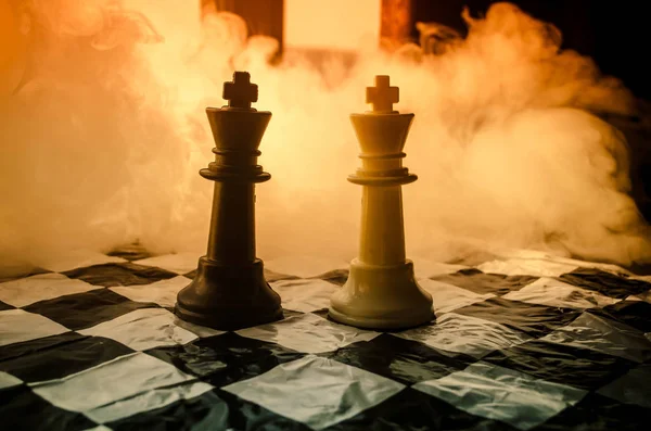 Концепция шахматной настольной игры бизнес-идей, конкуренции и стратегических идей. Шахматные фигуры на темном фоне с дымом и туманом и окном с солнечным светом . — стоковое фото