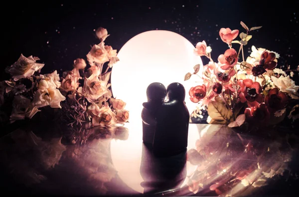 Dos muñecas abrazándose a la mesa con flores y decoración lunar Fondo iluminado con ahumado.Concepto de amor. Idea de diseño de tarjetas de felicitación o regalo. Un tono vintage. Silueta de abrazo pareja — Foto de Stock