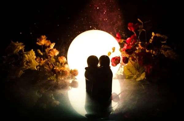 Dos muñecas abrazándose a la mesa con flores y decoración lunar Fondo iluminado con ahumado.Concepto de amor. Idea de diseño de tarjetas de felicitación o regalo. Un tono vintage. Silueta de abrazo pareja — Foto de Stock