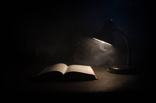 Open book near glowing table lamp on dark background, Lamp and opened book with smoke on background.
