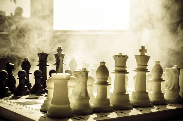 Концепция шахматной настольной игры бизнес-идей, конкуренции и стратегических идей. Шахматные фигуры на темном фоне с дымом и туманом. Выборочный фокус. Рука кладет фигуру на борт — стоковое фото