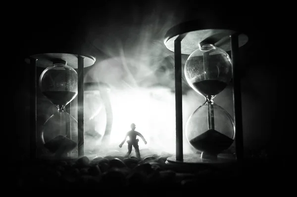 Έννοια του χρόνου. Σιλουέτα ενός ανθρώπου που στέκεται ανάμεσα σε κλεψύδρες με τον καπνό και τα φώτα σε σκούρο φόντο. — Φωτογραφία Αρχείου