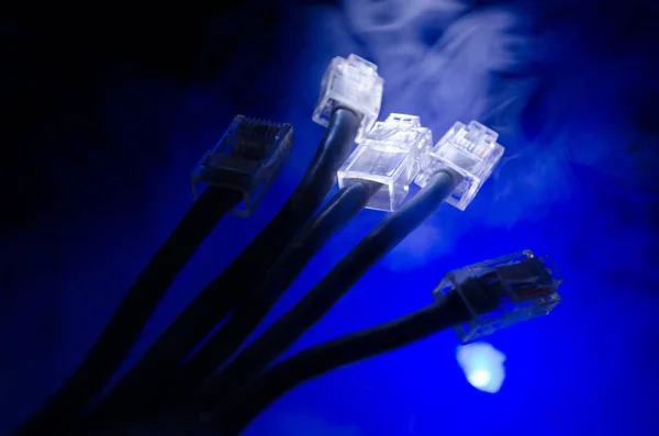 Interruptor de rede e cabos ethernet, símbolo de comunicações globais. Cabos de rede coloridos sobre fundo escuro com luzes e fumaça. Foco seletivo — Fotografia de Stock