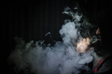 Bir mod tutarak Vaping adam. Buhar bulutu. Siyah arka plan. Vaping çok duman ile elektronik sigara