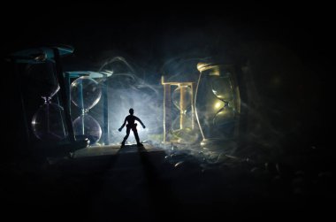 Zaman kavramı. Duman ile hourglasses ve karanlık bir arka plan ışıkları arasında duran bir adam silüeti.