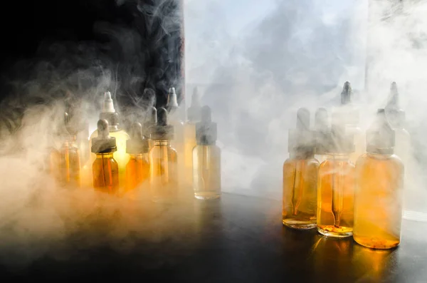 Concepto Vape. Nubes de humo y botellas de vapor líquido en la ventana con luz solar en el fondo. Efectos de luz. Útil como fondo o publicidad de vapor o fondo de vapor. De cerca. — Foto de Stock
