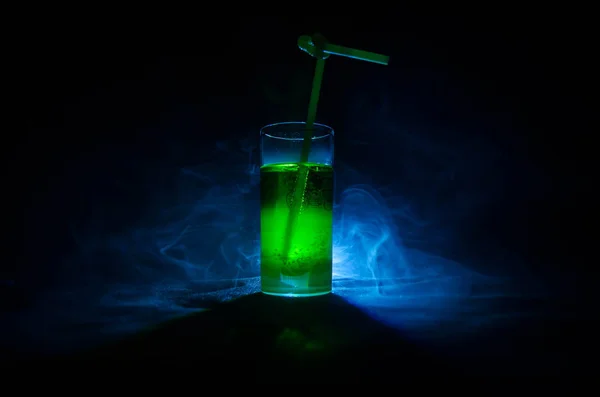 Vaso de cóctel verde con paja sobre fondo oscuro con humo y contraluz . — Foto de Stock