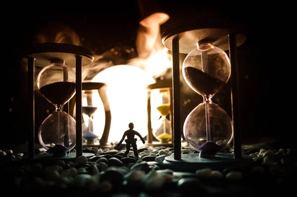 Zeitkonzept. Silhouette eines Mannes, der zwischen Sanduhren mit Rauch und Lichtern auf dunklem Hintergrund steht. — Stockfoto