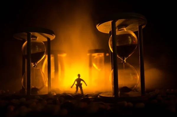 Time concept. Silhouette of a man standing between hourglasses with smoke and lights on a dark background. — Stock Photo, Image