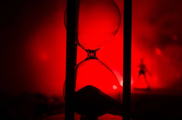 Концепция времени Силуэт человека, стоящего между песочными часами с дымом и огнями на темном фоне . — стоковое фото