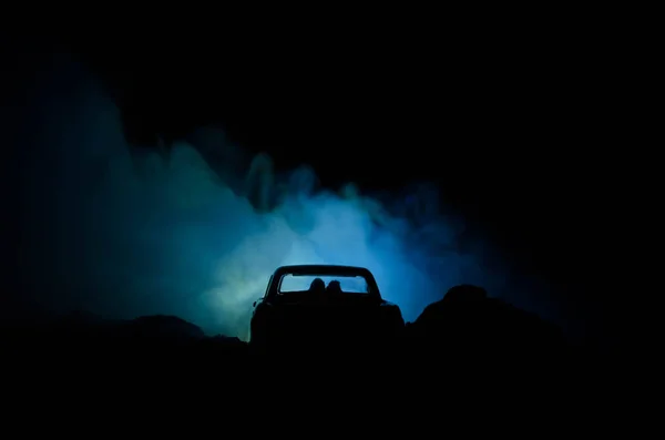 Silhouette eines Autos mit Pärchen drinnen auf dunklem Hintergrund mit Licht und Rauch. Romantische Szene. Liebeskonzept — Stockfoto