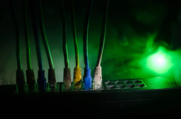 Conmutador de red y cables Ethernet, símbolo de las comunicaciones globales. Cables de red de color sobre fondo oscuro con luces y humo. Enfoque selectivo — Foto de Stock