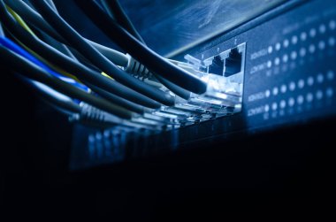 Ağ anahtarı ve ethernet kabloları, global iletişim sembolüdür. Işıklar ve duman ile koyu arka plan üzerinde renkli ağ kabloları. Seçici odak