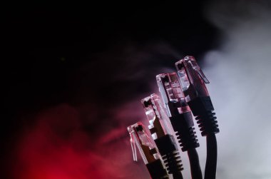 Ağ anahtarı ve ethernet kabloları, global iletişim sembolüdür. Işıklar ve duman ile koyu arka plan üzerinde renkli ağ kabloları. Seçici odak
