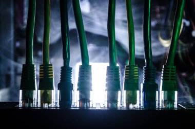 Ağ anahtarı ve ethernet kabloları, global iletişim sembolüdür. Işıklar ve duman ile koyu arka plan üzerinde renkli ağ kabloları. Seçici odak