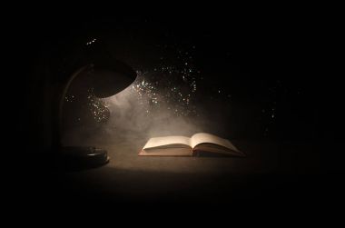 Koyu arka plan, lamba ve arka plan üzerinde duman ile açık kitap açık kitap parlayan masa lambası yakınındaki. Gerçeküstü