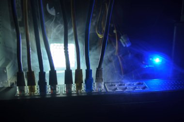 Ağ anahtarı ve ethernet kabloları, global iletişim sembolüdür. Işıklar ve duman ile koyu arka plan üzerinde renkli ağ kabloları. Seçici odak