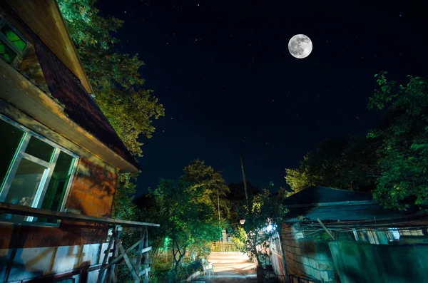 Schöne Landschaft Dorfstraße mit Gebäuden und Bäumen und großen Vollmond am Nachthimmel. Großer Kaukasus . — Stockfoto