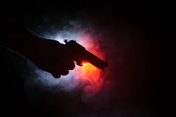 Pistola de mano masculina sobre fondo negro con luces traseras de color humo (amarillo anaranjado rojo blanco), concepto asesino de la mafia — Foto de Stock