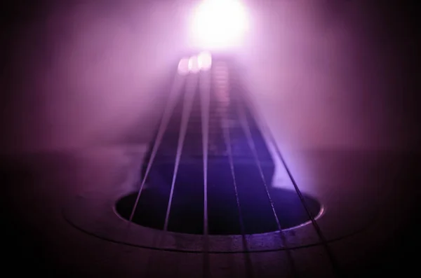 Music concept. Acoustic guitar isolated on a dark background under beam of light with smoke with copy space. Guitar Strings, close up. Selective focus. Fire effects