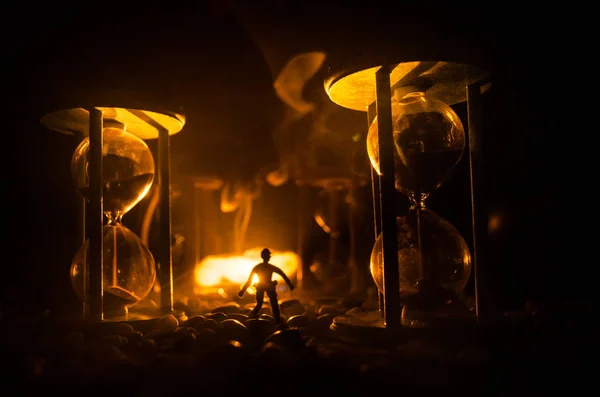 Concept du temps. Silhouette d'un homme debout entre des sabliers avec de la fumée et des lumières sur un fond sombre . — Photo