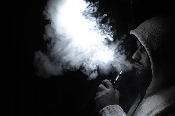 Vaping άνθρωπος που κρατά ένα mod. Ένα σύννεφο των ατμού. Μαύρο φόντο. Ηλεκτρονικό τσιγάρο με πολύ καπνό καπνίσματος — Φωτογραφία Αρχείου