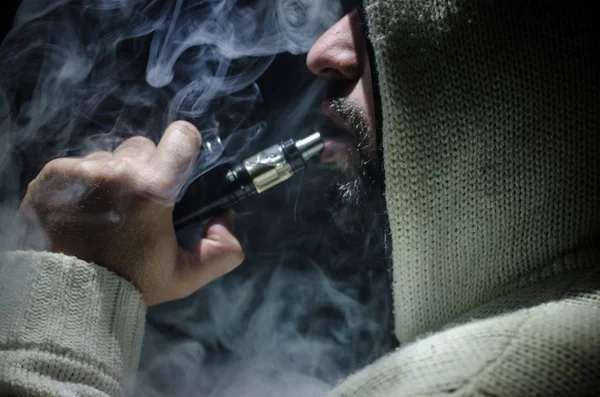 Vaping άνθρωπος που κρατά ένα mod. Ένα σύννεφο των ατμού. Μαύρο φόντο. Ηλεκτρονικό τσιγάρο με πολύ καπνό καπνίσματος — Φωτογραφία Αρχείου