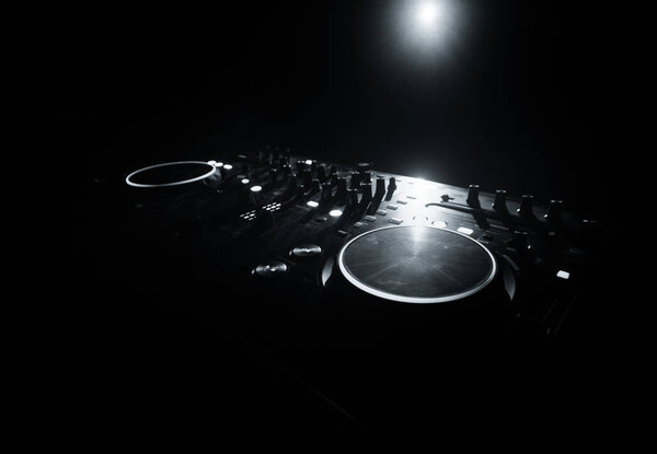 DJ Spinning, Mixing, and Scratching in a Night Club, Hands of dj tweak various track controls on dj's deck, strobe lights and fog, selective focus