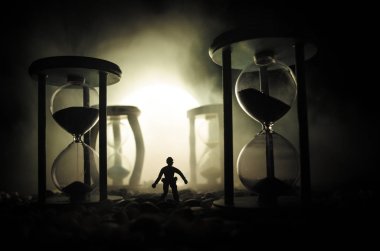 Zaman kavramı. Duman ile hourglasses ve karanlık bir arka plan ışıkları arasında duran bir adam silüeti.