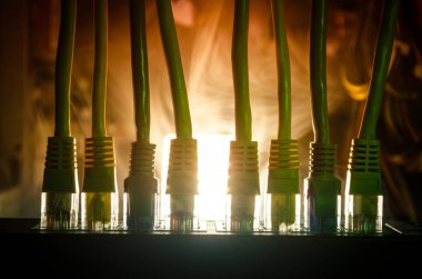Ağ anahtarı ve ethernet kabloları, global iletişim sembolüdür. Işıklar ve duman ile koyu arka plan üzerinde renkli ağ kabloları. Seçici odak
