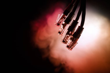 Ağ anahtarı ve ethernet kabloları, global iletişim sembolüdür. Işıklar ve duman ile koyu arka plan üzerinde renkli ağ kabloları. Seçici odak