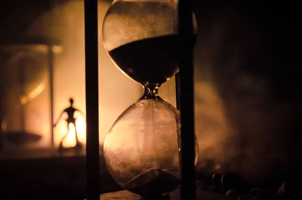 Zaman kavramı. Duman ile hourglasses ve karanlık bir arka plan ışıkları arasında duran bir adam silüeti. — Stok fotoğraf
