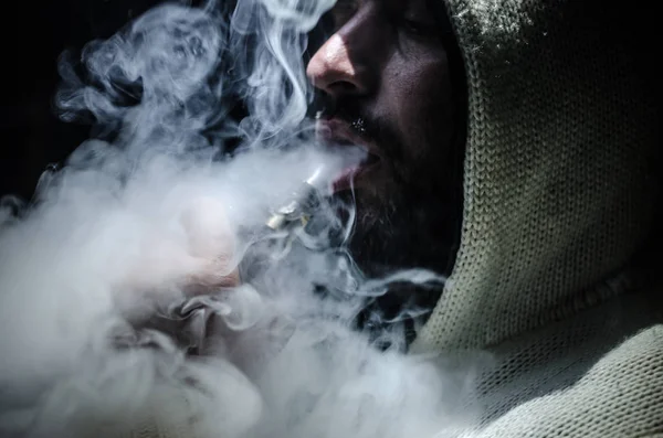 Hombre aspirante sosteniendo un mod. Una nube de vapor. Fondo negro. Vapeando un cigarrillo electrónico con mucho humo —  Fotos de Stock