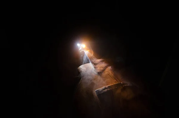 Music concept. Acoustic guitar isolated on a dark background under beam of light with smoke with copy space. Guitar Strings, close up. Selective focus. Fire effects