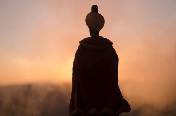 Silhouette de l'homme arabe se tient seul dans le désert et regarder le coucher du soleil avec des nuages de brouillard. Conte de fées oriental — Photo