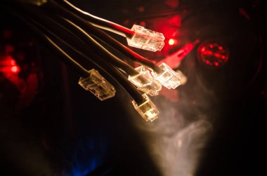 Ağ anahtarı ve ethernet kabloları, global iletişim sembolüdür. Işıklar ve duman ile koyu arka plan üzerinde renkli ağ kabloları. Seçici odak