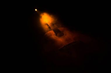 Müzik konsepti. Akustik gitar ile kopya alanı dumanla ışık demeti altında karanlık bir arka plan üzerinde izole. Gitar telleri, yakın çekim. Seçici odak. Yangın etkileri