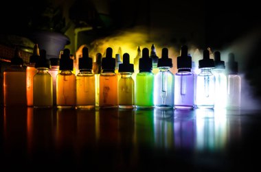 Vape konsepti. Karanlık arka planda duman bulutları ve tüp sıvısı şişeleri. Işık efektleri. Arka plan, vape reklamı ya da vape arkaplan olarak kullanışlı. Seçici odak