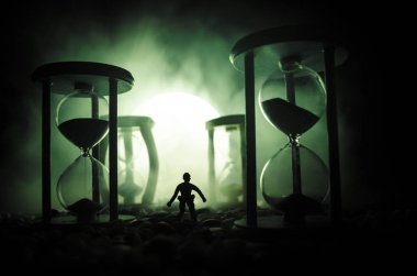 Zaman kavramı. Duman ile hourglasses ve karanlık bir arka plan ışıkları arasında duran bir adam silüeti.