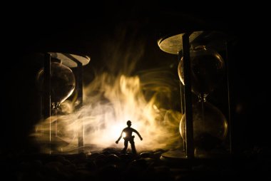 Zaman kavramı. Duman ile hourglasses ve karanlık bir arka plan ışıkları arasında duran bir adam silüeti.